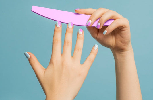 Imagen de un par de manos femeninas, con uñas decoradas con esmalte tipo gelish. La mano derecha sostiene una lima de uñas.